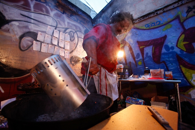 Artist Brent Holmes adds coal to a grill during his "Sin Eater" food-based performance art piece as part of "The Traveling Miracle Show" at Momas and Dadas New Genres Project House, 926b S. Casino ...