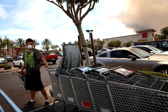 Jason Moore, 17, wears a mask protect to himself from the smoke produced by the Carpenter 1 fire, seen in background at right, while working in northwest Las Vegas Tuesday. The wildfire, which has ...