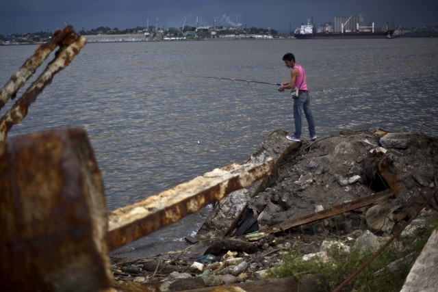 In this Sept. 9 photo, a man fishes in an area where debris was extracted from the seabed at the harbor across the water from a refinery in Havana, Cuba. Havana's harbor has long been a jumble of  ...