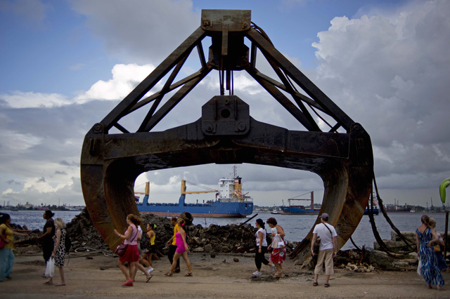 In this Aug. 20 photo, tourists walk past an excavator shovel at the harbor of Havana, Cuba. Havana's harbor has long been a jumble of piers left to crumble into piles of rusty, twisted rebar. But ...