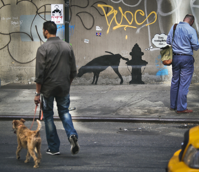 Graffiti by the secretive British artist Banksy, featuring a dog and a fire plug, draws attention on 24th Street, near Sixth Avenue in New York, on Friday, Oct. 4, 2013. Banksy graffiti is turnin ...