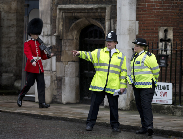 Police officers monitor the small crowd of media and royal fans outside St. James's Palace as a member of the Grenadier Guards marches past in London on Wednesday. Queen Elizabeth II and her husba ...
