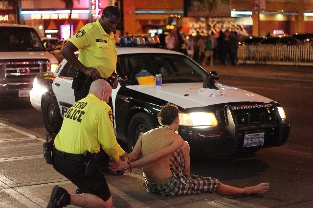 Metro Police officers detain and search a man stopped for walking with an open alcohol container in the Fremont East entertainment district in Las Vegas on Aug. 2. (LAS VEGAS REVIEW-JOURNAL)