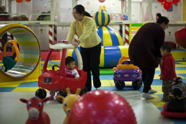 Parents play with their children at a kid's play area in a shopping mall in Beijing in January. China will loosen its decades-old one-child policy and abolish a much-criticized labor camp system, ...