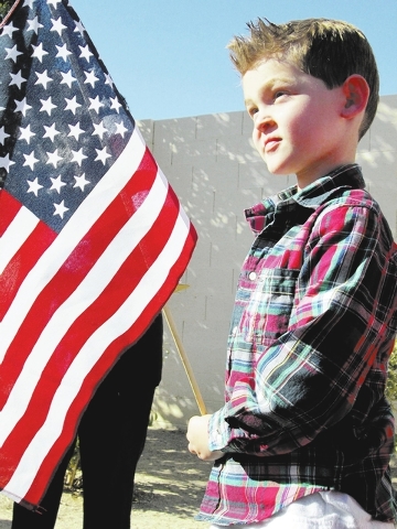 Phillip Smith, 5, holds a flag while students say the Pledge of Allegiance, Nov. 8 at the Merryhill School, 7065 Grand Teton Drive. Students presented handmade cards to current and retired militar ...
