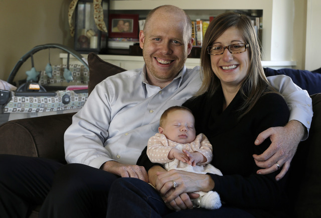 In this photograph taken Thursday, Nov. 21, 2013, Ken Ernst, left, and his wife Abigail Ernst, right, pose for The Associated Press with their 2-month-old daughter, Lucy, in their Oldwick, N.J. ho ...