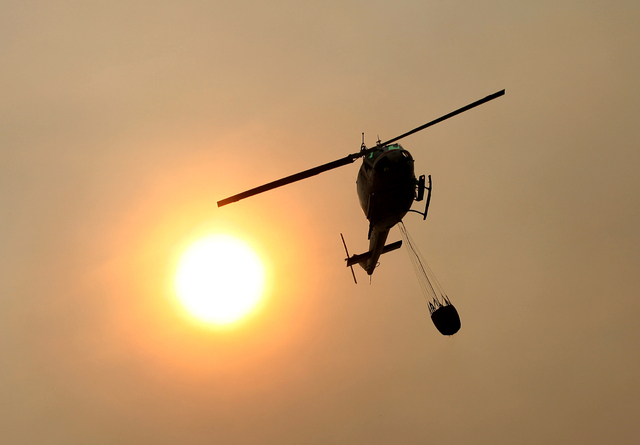 A Cal Fire helicopter flies over Pfeiffer Ridge on Monday, Dec. 16, 2013, in Big Sur, Calif. The wildfire burning Monday in the Big Sur area of California destroyed at least 15 homes and forced ab ...