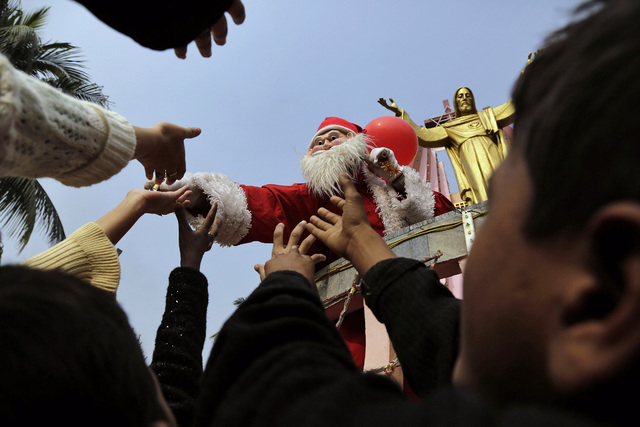 A man dressed as Santa Claus distributes sweets to children on the occasion of Christmas outside a church in Gauhati, India, Wednesday, Dec. 25, 2013. Although Christians comprise only two percent ...