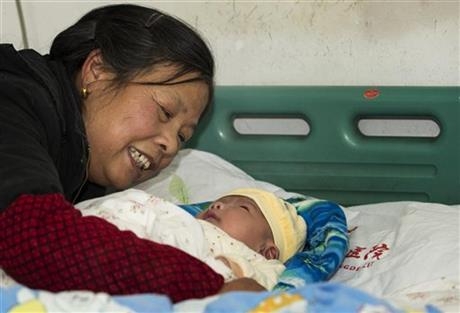In this photo taken Thursday Dec. 12, 2013, a woman tries to cheer up her grandson who is recovering from serious adverse reaction to hepatitis B vaccination in a hospital in Changde city in south ...