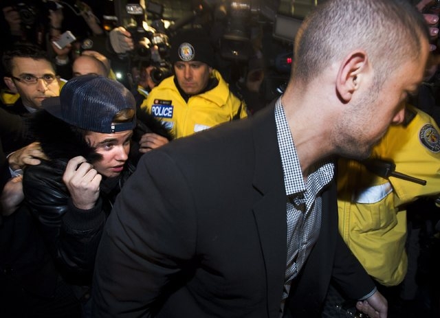 Canadian musician Justin Bieber is swarmed by media and police officers as he turns himself into city police for an expected assault charge, in Toronto, on Wednesday, Jan. 29, 2014. A police offic ...