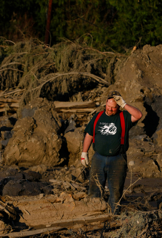 Jason Anderson searches through mudslide rubble for bodies on Cory Kuntz's property on Sunday. The Kuntz family had gone to a baseball game Saturday morning when the fatal slide swept through the ...