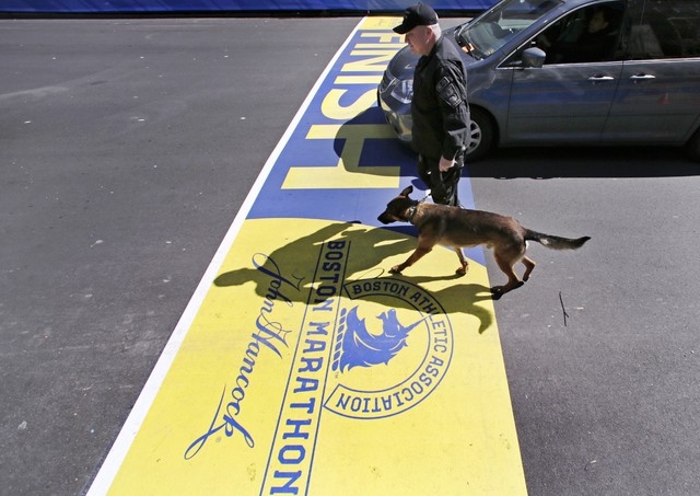 Boston Police officer John Quinn walks with Miller, his bomb detection canine, over the finish line while sweeping the area in preparation for the Boston Marathon, Wednesday, April 16, 2014, in Bo ...