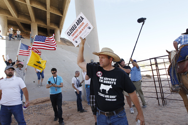 Ammon Bundy, middle, son of rancher Cliven Bundy, removes a "closed area" sign from the BLM impound corral after the BLM agreed to release his family's a cattle near Bunkerville on April ...