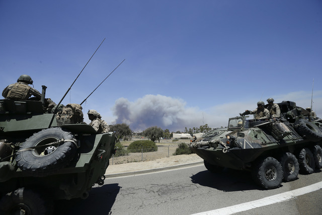 Marines move military vehicles near the entrance to Marine Corps Camp Pendleton in front of smoke plumes from the Las Pulgas wildfire burning on base Friday, May 16, 2014, in Oceanside, Calif. San ...