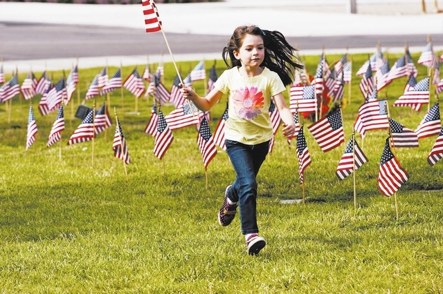 7 year old Ashley Hall runs through the Southern Nevada Veterans Cemetery carrying an American flag Saturday May 24, 2014. Over twenty thousand flags were placed this morning by the Disabled Ameri ...