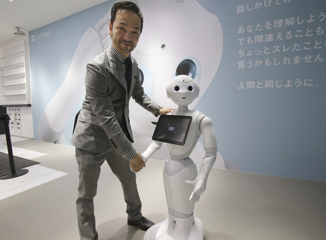 Kaname Hayashi, project leader of Humanoid Robot "Pepper" poses for photos with "Pepper" at SoftBank Mobile shop in Tokyo, Friday, June 6, 2014. Pepper, which has no hair but two large doll-like e ...