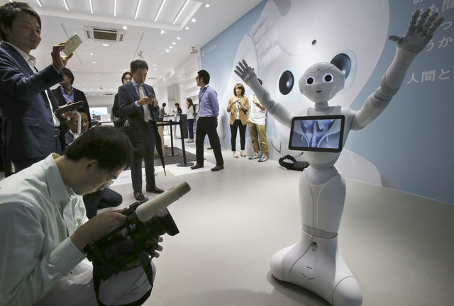 Members of press surround humanoid Robot "Pepper" on display at SoftBank Mobile shop in Tokyo, Friday, June 6, 2014. Pepper, which has no hair but two large doll-like eyes and a flat-panel display ...