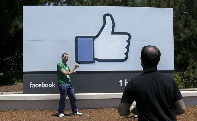 In this June 11, 2014 photo, a man poses for photographs in front of the Facebook sign on the Facebook campus in Menlo Park, Calif. In the coming weeks, Facebook will start offering advertisers an ...