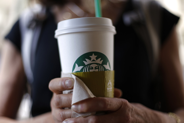 Aa woman holds a coffee drink outside a Starbucks in downtown Chicago. Starbucks is raising prices on some of its drinks by 5 cents to 20 cents starting next week, and customers can also soon expe ...