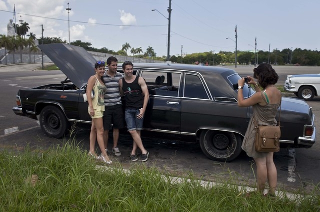 In this June 18, 2014 photo, tourists from Barcelona, Spain take a picture with a Soviet-made limousine taxi cab that once belonged to Fidel Castro's fleet in front of Revolution Plaza in Havana, ...
