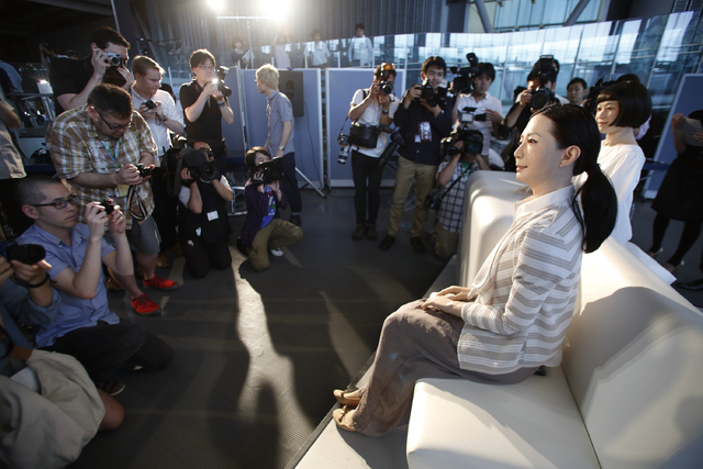 Photographers gather around to take photos of a female-announcer robot called Otonaroid, second right, and a girl robot called Kodomoroid, right, during a press unveiling of new guides at the Nati ...