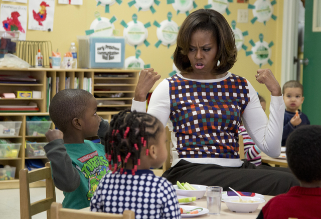 FILE - In this Feb. 27, 2014 file photo first lady Michelle Obama and a young student show off their muscles as they eat healthy snacks during a visit to La Petite Academy in Bowie, Md., to encour ...