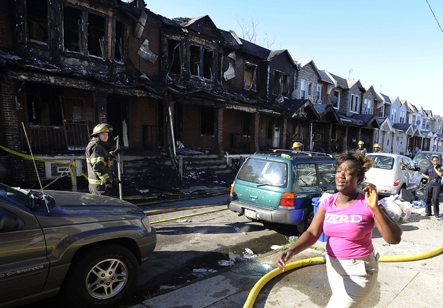A woman cries as she walks past Philadelphia firefighters working on burned row homes on Saturday, July 5, 2014, in Philadelphia. A fast-moving fire in southwest Philadelphia early Saturday left f ...