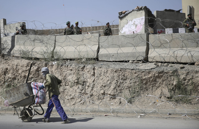 An Afghan laborer walks past a gate of Camp Qargha as Afghanistan National Army soldiers stand guard, west of  Kabul, Afghanistan, Tuesday, Aug. 5, 2014. A man dressed in an Afghan army uniform op ...
