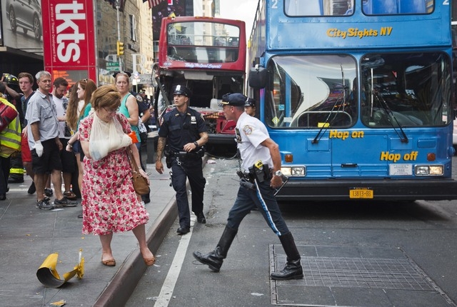 A woman, her arm bandaged and in a sling, leaves after being treated at the scene of a traffic accident apparently involving two double-decker tour buses in New York's Times Square, Tuesday Aug. 5 ...