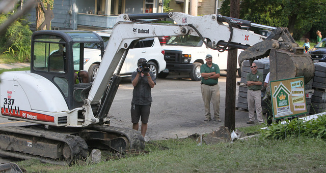 LeBron James operates an excavator as a camera operator and Darren Rowland and Brian Rice of Rice Nursery and Landscaping, look on at a rehab site on Monday, Aug. 4, 2014, in Akron, Ohio. His sons ...