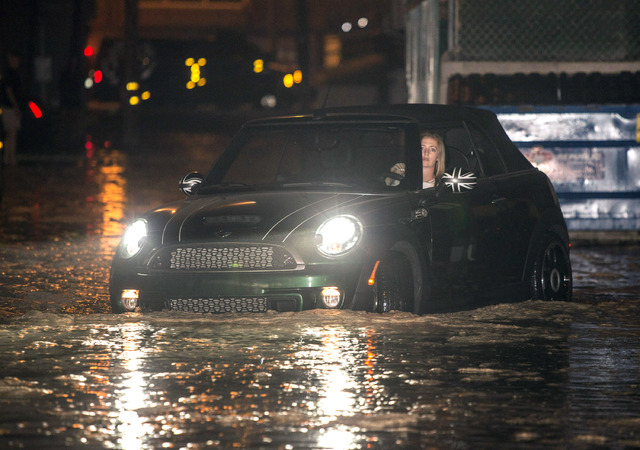 A woman drives through a flooded street after high tide and large waves caused heavy flooding in Seal Beach, California, Tuesday, Aug. 26, 2014. A low-lying street in the Southern California coast ...