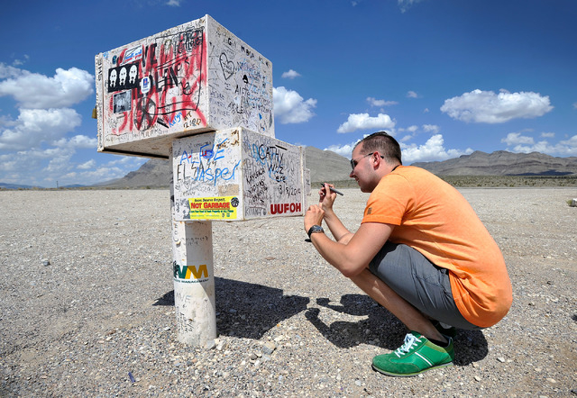 Floris Otten, of The Netherlands leaves a message on the famous black mailbox along Nevada Highway 375 or Extraterrestrial Highway, on Tuesday, Aug. 5, 2014. The mailbox, which is now white and ow ...
