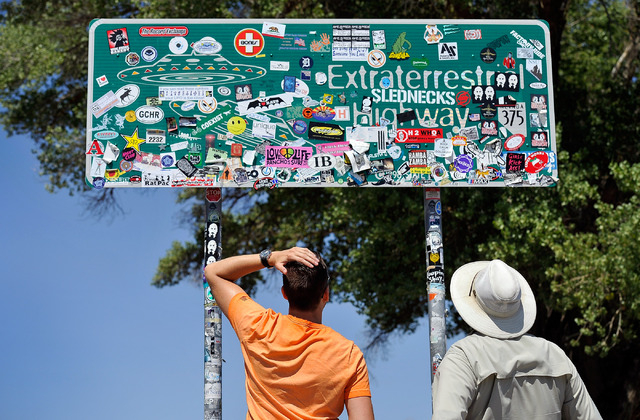 Tourist Floris Otten, left, of The Netherlands, and Dean Baumgartner, of Adventure Photo Tours look over all the stickers covering the Extraterrestrial Highway sign on Tuesday, Aug. 5, 2014. Baumg ...