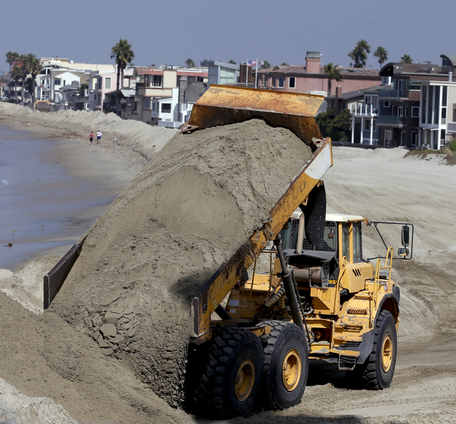 A dump truck works to pile sand on a temporary berm to protect beach front homes on, Friday, Sept. 5, 2014, in Long Beach, Calif. Southern California is in for another round of high surf generated ...