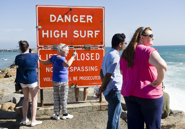 A sign warns visitors of high surf as they stand on the jetty protecting Dana Point Harbor on Saturday afternoon Sept. 6, 2014 in Dana Point, California. Hurricane Norbert in Baja California is re ...