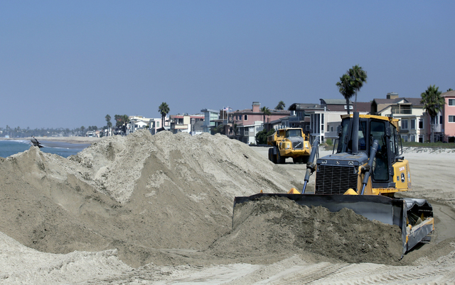 A bulldozer works to pile sand on a temporary berm to protect beach front homes on, Friday, Sept. 5, 2014, in Long Beach, Calif. Southern California is in for another round of high surf generated ...
