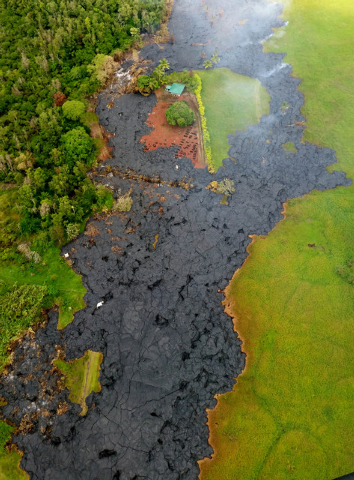In this Oct. 28, 2014 photo provided by Pete Stachowicz of Paradise Helicopters, lava flow has partially buried a cemetery, top center, near the town of Pahoa on the Big Island of Hawaii. The Nati ...
