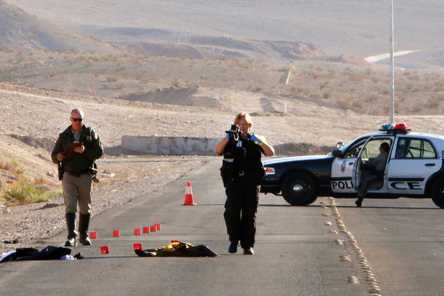 A Las Vegas police accident scene photographer takes a picture at the accident scene Friday, Oct. 31, 2014, near Sahara Avenue and Hollywood Boulevard. Two men sitting on the trunk of a car driven ...