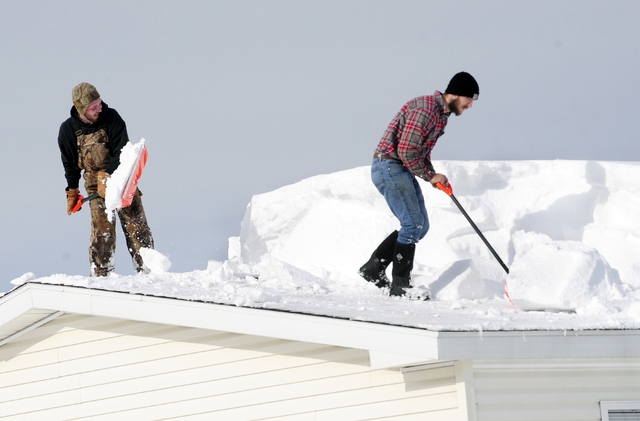 D.J. Schloss, left, and Doug Metz shovel off a roof on Abbey Lane in Alden, N.Y., Thursday, Nov. 20, 2014. The weight of the snow has caused problems around the area with roofs collapsing and buil ...