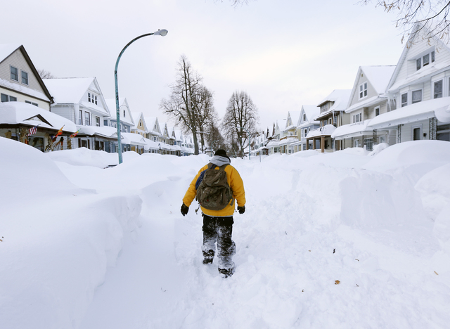Brian Cintron walks in his snow-bound south Buffalo, N.Y., neighborhood on Thursday, Nov. 20, 2014. A new blast of lake-effect snow pounded Buffalo for a third day, piling more misery on a city al ...