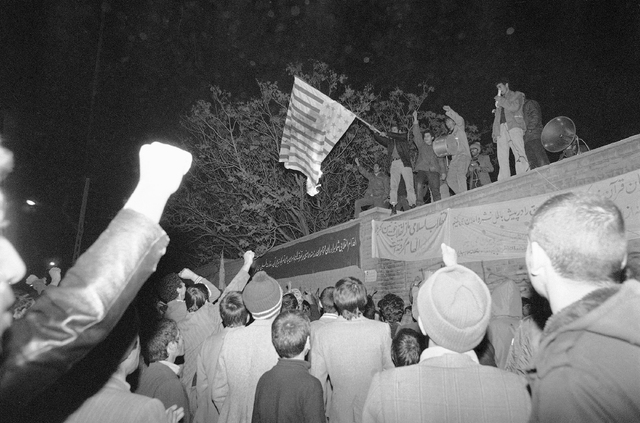 Crowd watch as the Stars and Stripes is burned by demonstrators atop of the non-functioning U.S. consulate in Tehran, Iran, on Dec. 17, 1979. (AP Photo)
