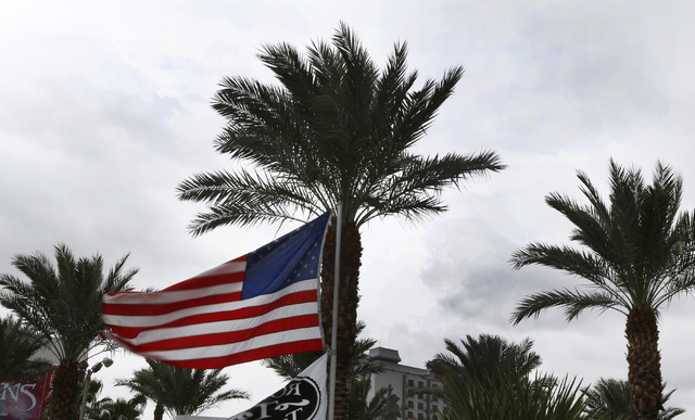 U.S. flag and palm trees blow in the wind against dark sky on the Las Vegas Strip near the MGM Grand as heavy rain approaches the Las Vegas Valley on Friday, Dec. 12, 2014. A weather system that i ...
