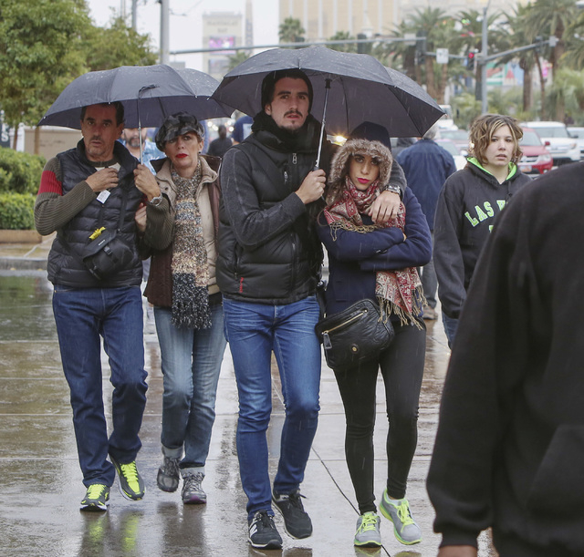 Pedestrians holding umbrellas walk on the side walk along Las Vegas Boulvard near Aria Hotel and Casino as heavy rain approaches the Las Vegas Valley on Friday, Dec. 12, 2014. A weather system tha ...