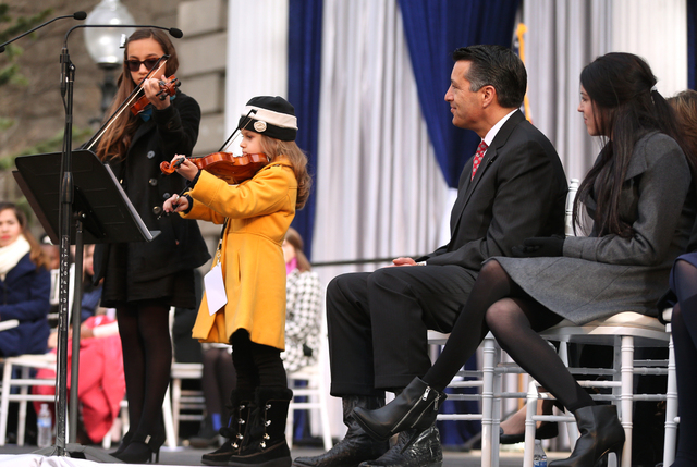 Gov. Brian Sandoval and his daughter Maddy, right, listen to a performance of "Home Means Nevada" by Alexia Ciobanu, 7, and Haylee Reynolds, 13, during the inauguration on the steps of t ...