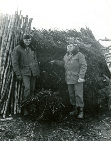U.S. Army Air Corps officers, Col. Frank Krebs, left, and Maj. Howard Cannon, pose next to a wood pile hidey hole, where the two pilots and Sgt. (no name given) Broga, not shown, hid from German s ...