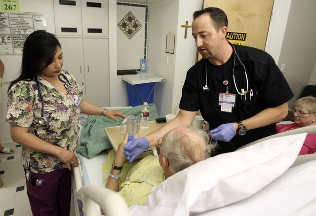 Registered Nurse Rachel Chao, left, trains new RN graduate Christian Perrodin with patient Cliff Walter of Henderson at Walter's wife, Nancy Walter waits at Saint Rose Dominican Siena Wednesday, J ...