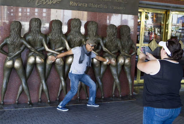 A man poises for a photo with the Crazy Girls statue in front of