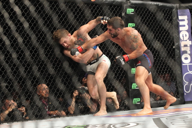 Chad Mendes, right, attacks Conor McGregor against the cage during their interim featherweight title bout at UFC 189 at the MGM Grand Garden Arena Saturday, July 11, 2015, in Las Vegas. McGregor w ...