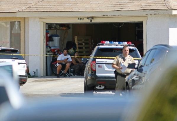 People sit in a garage at a home located in the 6900 block of Berkshire Place Friday, Aug. 7, 2015, in Las Vegas. Police checking reports of a broken window shot and killed a man who lunged at off ...