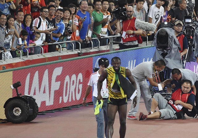 Usain Bolt of Jamaica (front R) limps after being knocked over by a cameraman (R) on a Segway after winning the men‘s 200 metres final at the 15th IAAF World Championships at the National St ...